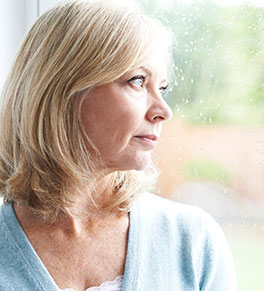 A middle-aged woman looks sad as she gazes out a window.