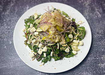 Golden harvest pear salad displayed on a white plate that sits on a concrete counter.