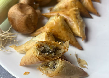 Leek and mushroom phyllo triangles are displayed on a white plate with one cut open to see inside.