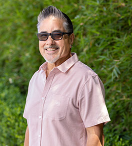 Gastric cancer survivor Mauricio Alvarez, pictured in a pink shirt and dark-framed glasses, stands in front of the UCI Health Chao Digestive Disease Center in Orange.