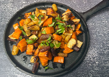 Sriracha honey roasted root vegetables are piled onto a cast iron skillet ready to be served.