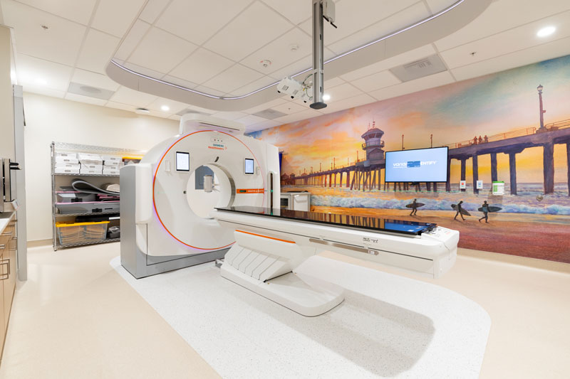 a mural of the huntington beach pier lines the wall of a room with a CT scanner at UCI Health irvine