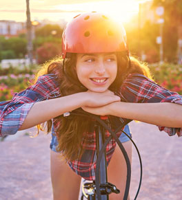 an adolescent girl wearing a bike helmet while posing with her electric bike as the sun sets behind her