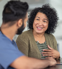 a women visits urgent care complaining of chest pain and holds her chest while a man in scrubs listens to her speak