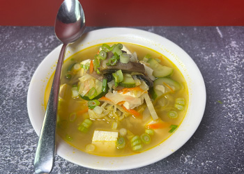 Hearty vegetable and chicken miso soup served in a white bowl with a spoon balanced on the left side.