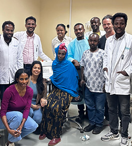 UCI Health radiation oncologist Dr. Priya Mitra kneels to next to the first patient to receive brachytherapy treatment at the Jimma University Oncology Center in Ethiopia. They are flanked by staff at the center along with three Radiating Hope volunteers.