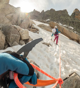 A couple hiking in snow-covered mountains while roped together and wearing a helmet for safety