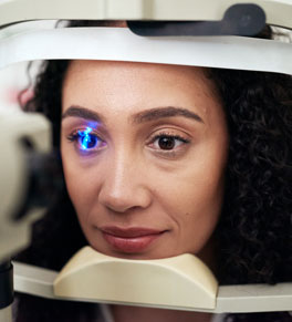a woman with curly brown hair gets her right eye screened for glaucoma with a blue laser