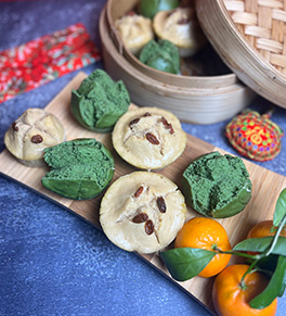 Six multi-colored Chinese prosperity cakes are displayed on a bamboo board set on blue cloth with red decorations.