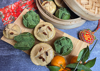 Chinese prosperity cakes are displayed on a bamboo board placed on a blue cloth with a bamboo steamer in the background.