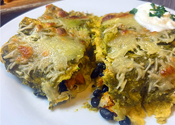 Black bean and sweet potato enchiladas are cut in half to show the filling and topped with sour cream and cilantro.