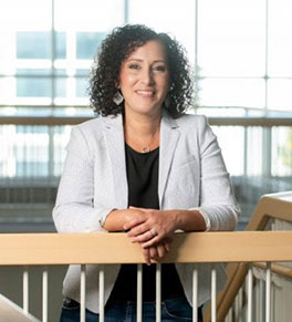 Selma Masri, an associate professor of biological chemistry at UC Irvine, pictured in a white jacket in the Falling Leavings medical innovation building.
