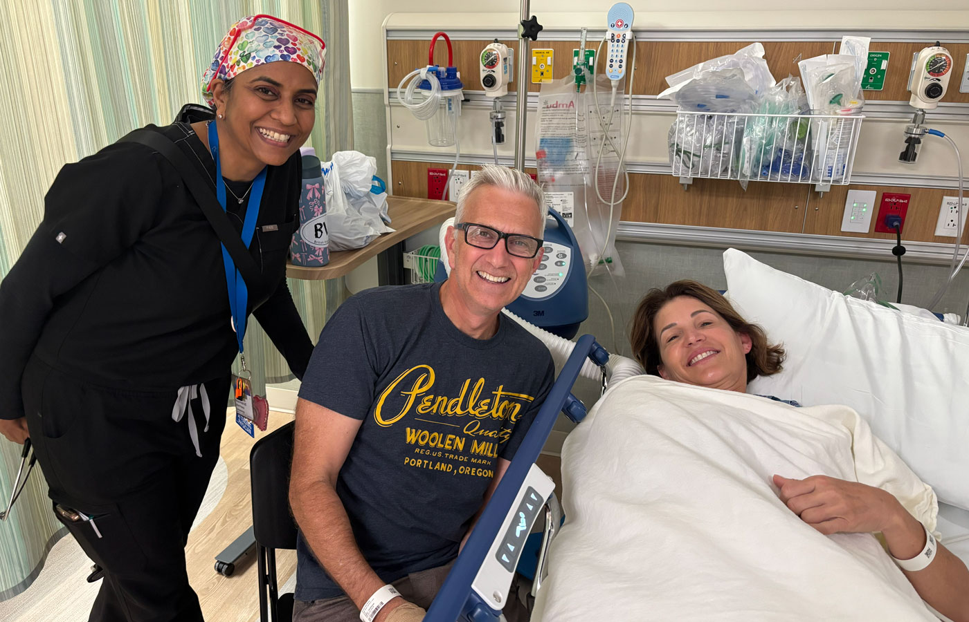 uci health gastroenterologist takes a photo with uci health anesthesiologist dr cameron ricks and his wife michelle malchiodi, laying in bed, after their colonoscopies together