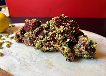 Citrus-coriander roasted beets are covered in a pumpkin seed gremolata and served on a marble cutting board.