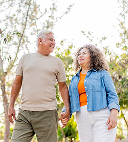 An older couple are holding hands and smiling as they take a walk in nature.
