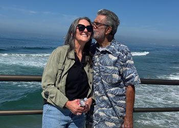 bob "the greek" bolen on the huntington beach pier on a sunny day giving a kiss to his daughter on the cheek