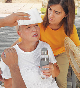 People are helping a mature woman who is suffering from heat stroke, giving her a cold compress and water.