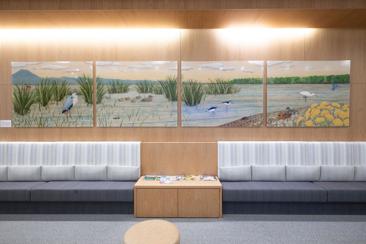 a multimedia mural – “The Story of the Marsh by Karen Wilkie - features marsh grass and ducks on a wall over seating. the painting is in the wen center.