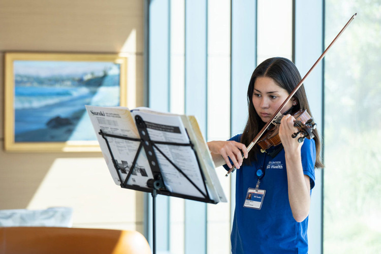 a uci health volunteer wearing a blue shirt plays the violin for patients and visitors at the chao family comprehensive cancer center 