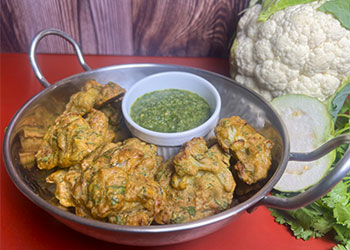 Air-friend cauliflower pakoras are displayed in a stainless steel wok with guava mint chutney in a white side dish.