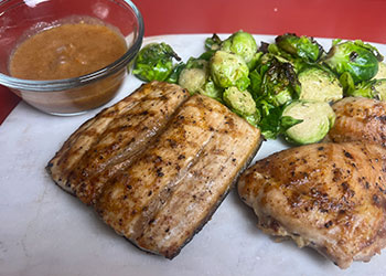 Two pieces of mahi mahi, a glass bowl of guava mint glaze and roasted brussel sprouts are displayed on a white marble cutting board.