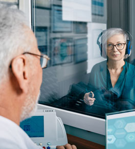 a woman sits in a room wearing headphones getting a hearing test in front of a male audiologist