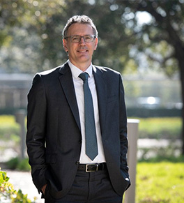 Dr. Diego A. Pizzagalli smiling and wearing a black suit with blue tie, stands on the UC Irvine campus.