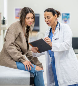 a young woman on an exam table speaking to her doctor in a brightly lit clinic room