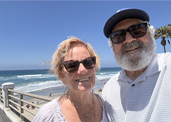 Kathi and Dominick Maggio are smiling on a sunny day with Huntington Beach in the background.