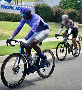 Blake Hoard is seated on his racing bike, dressed in a purple helmet and shirt and white bike shorts.