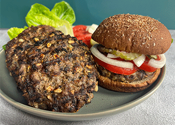 Juicy mushroom and beef burgers are displayed on green plate with lettuce and tomato in the background.
