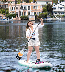 Tiphany Kane, in swim shorts and white blouse, paddleboards near her Mission Viejo home.