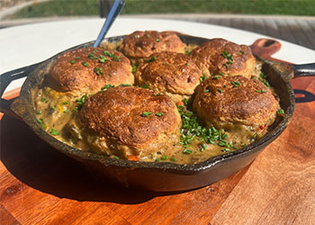 Chicken pot pie with whole grain biscuits is served in a cast iron skillet that is sitting on a wood carving board.