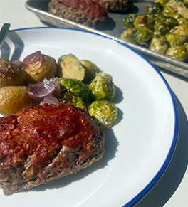 Sheet pan mini meatloves are displayed with roasted Brussels sprouts and rosemary potatoes on a blue rimmed white plate.