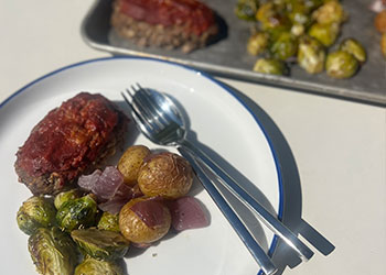 An overhead view of sheet pan mini meatloaves with rosemary potatoes and roasted Brussels sprouts served on a blue rimmed white plate.