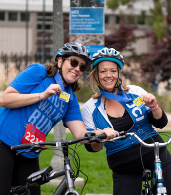 two female cyclists on their bikes wearing helmets smiling at the uc irvine anti cancer challenge bike walk ride