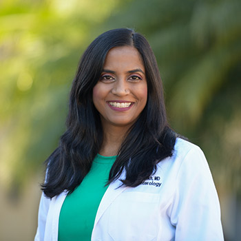 Gastroenterologist Dr. Nimisha Parekh, wearing a white coat in front of green trees, is the founder and director of the UCI Health SHE program and director of the Digestive Health Institute's Inflammatory Bowel Disease Program."