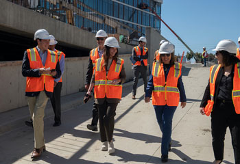 california lieutenant governor eleni kounalakis in orange safety vest with group of people walking and touring the uci health irvine campus under construction