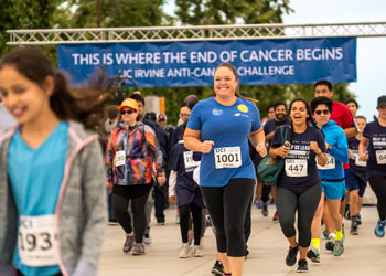 group of competitors at the uci anti-cancer challenge in 2019 wearing uci blue in front of a sign saying "this is where the end of cancer begins". the challenge has funded 100 research projects to find a cure for cancer.