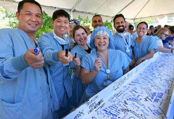uci health coworkers in blue scrubs smiling at a beam signing event for uci medical center before installation at uci health -- irvine