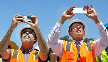 uci health ceo chad lefteris, left, and uci school of medicine dean dr. michael stamos, wearing orange vests and hard hats hold up their phones to take photos and video of the topping off ceremony at uci health
