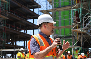 uci health ceo chad lefteris addresses construction workers at uci health irvine wearing orange vest and hard hat holding microphone in front of a blue sky
