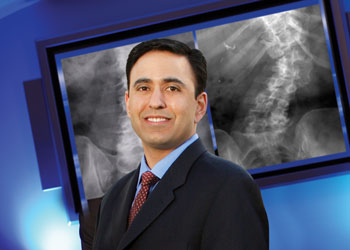 uci health spine surgeon dr. nitin bhatia in dark suit and burgundy tie standing in front of x-ray; bhatia spoke to becker's about what spine surgeons should be doing for patients