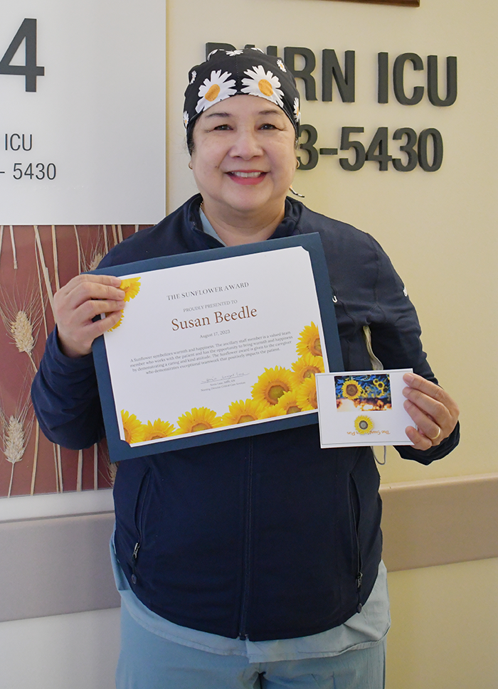 uci health burn unit nursing assistant susan beedle wearing scrubs, holding SUNFLOWER award and smiling