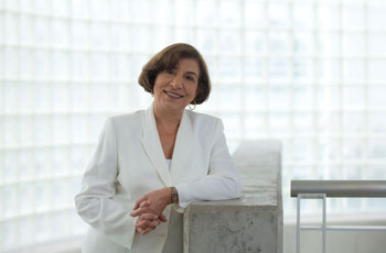 claudia kawas in white coat standing in front of window