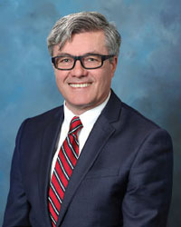 dr adrian preda american psychiatric association in front of a blue background wearing a dark suit white shirt and red and blue striped tie