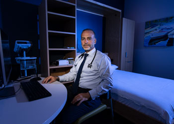 uci health sleep medicine specialist dr. rami khayat in his office wearing a stethoscope and sitting on an exam bed bathed in blue light; dr khayat explains the importance of REM sleep