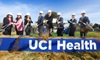 uci health executive leadership at the uci health rehabilitation hospital groundbreaking wearing white hard hats and shoveling dirt behind a blue sign reading uci health in white letters