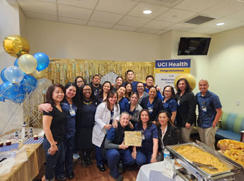 the medical intensive care unit team celebrates their gold level beacon award, which one person is holding, in a conference room with balloons, streamers and food