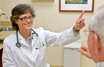 uci health geriatrician lisa gibbs wearing a white coat and stethoscope works with an elderly man with white hair and glasses in a medical office